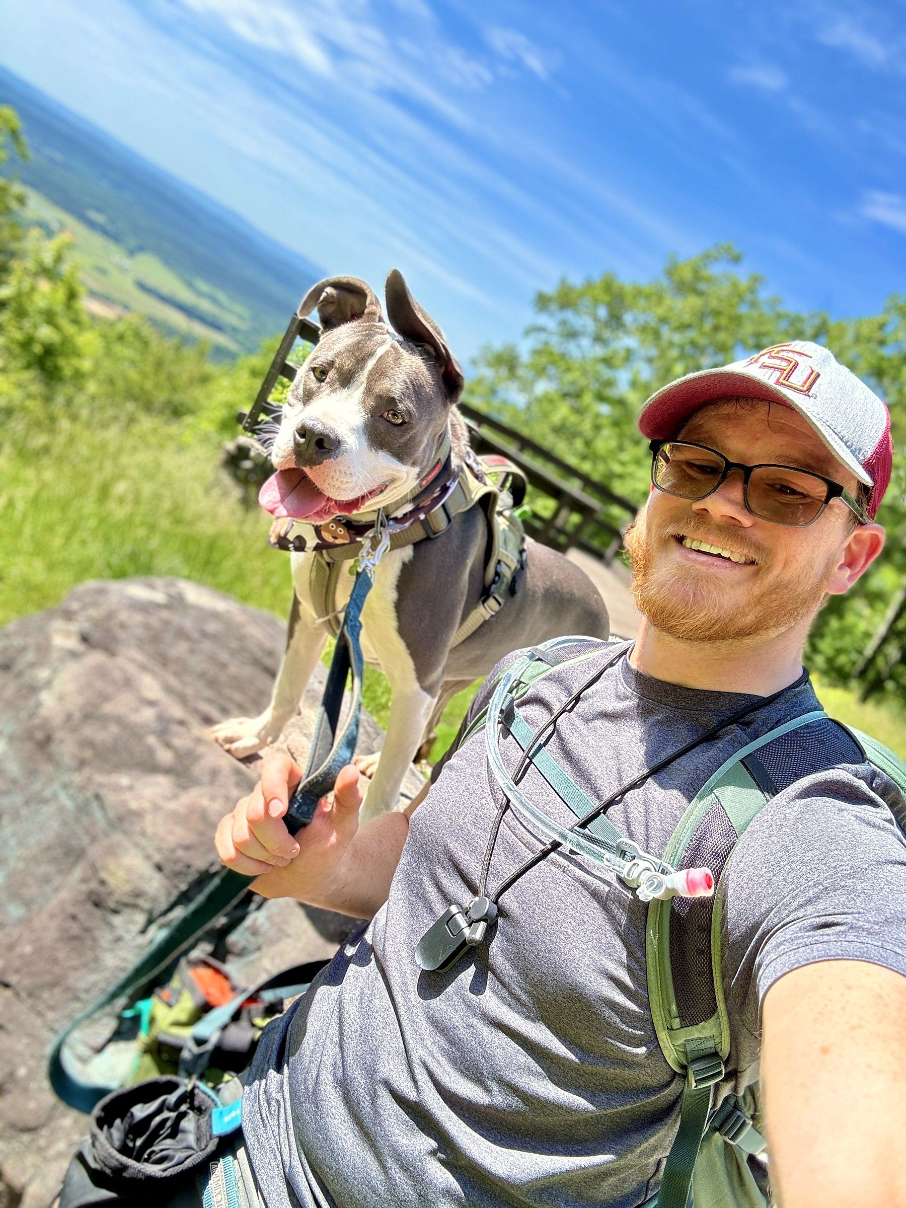 Phillip Greene and Lucky on a rocky summit overlook, both squinting into the sun